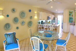 A modern kitchen with white cabinets, a stainless steel refrigerator, and a dining area with a glass table and white chairs. - Terrasol Oceanview Condo with Patio (Cabo San Lucas)