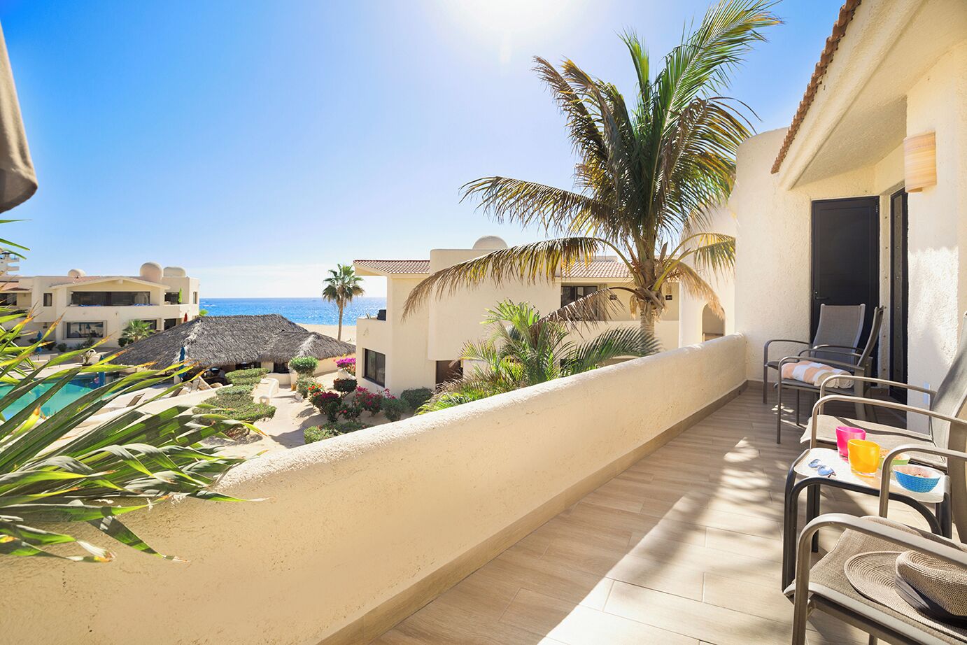 A balcony with a pool, palm trees, and a view of the sea.