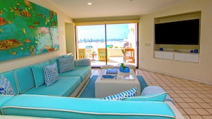 A living room with a teal sofa, a coffee table, and a large painting of fish. - Terrasol Oceanview Condo with Patio (Cabo San Lucas)