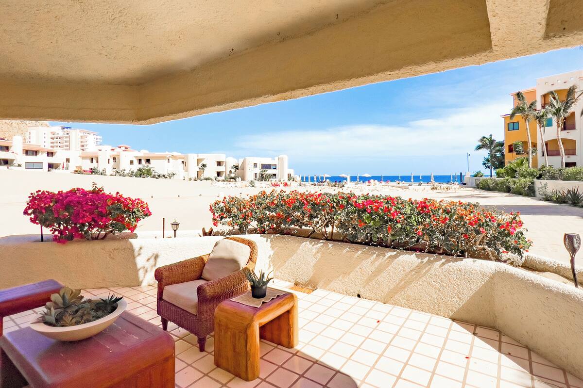 Ein Balkon mit Korbmöbeln, einem Blumentopf und einem Blumenbeet mit roten Blüten.