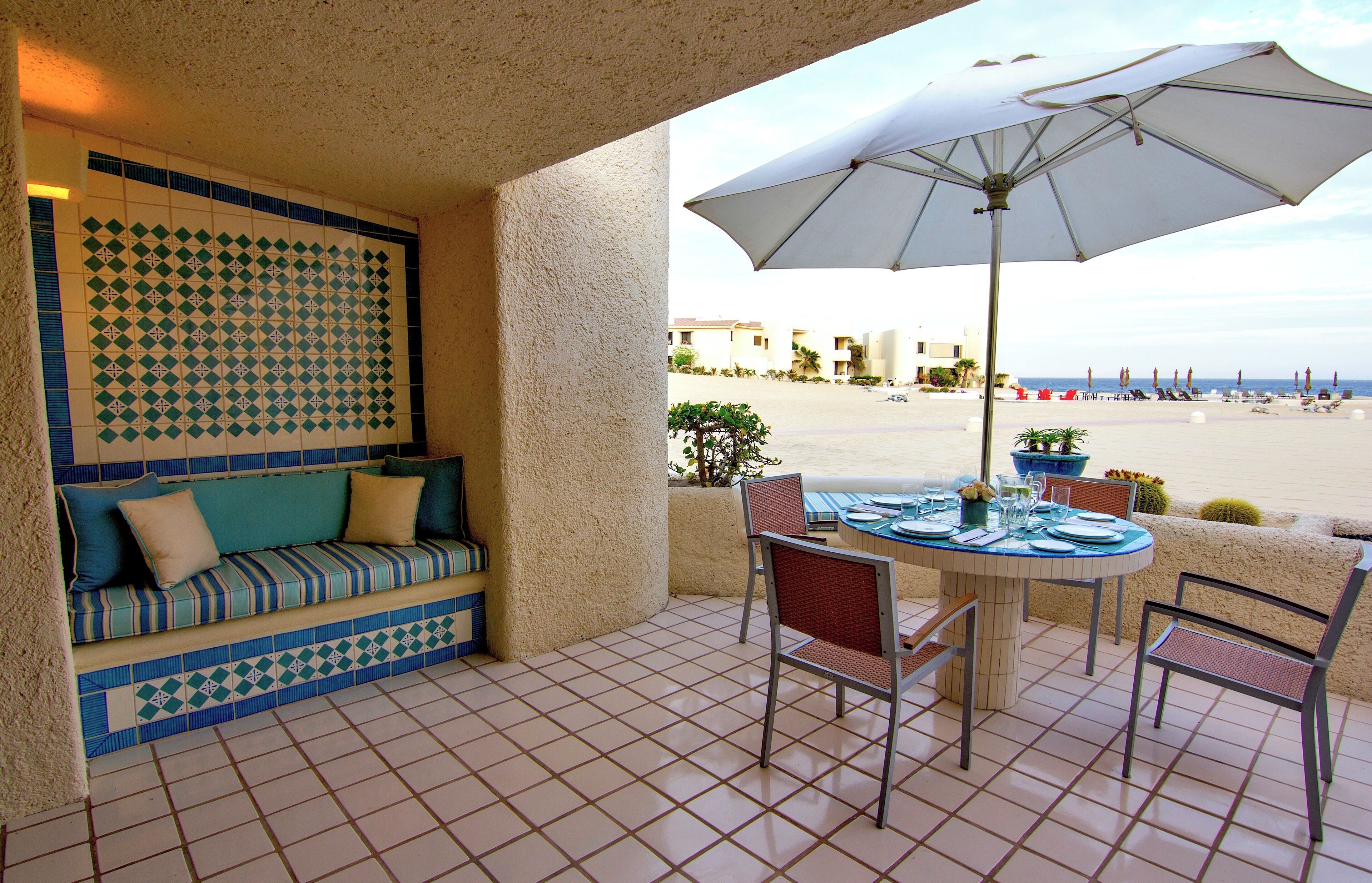 Een terras met betegelde vloer, een comfortabele bank, een tafel met stoelen en een parasol.