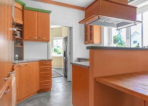 A kitchen with wooden cabinets, a countertop, and a window with a view of greenery outside. - Beautiful Room in Shared Villa | Garden & Parking (Wien)