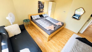 Una habitación con cama, una mesita, un ventilador y un espejo.