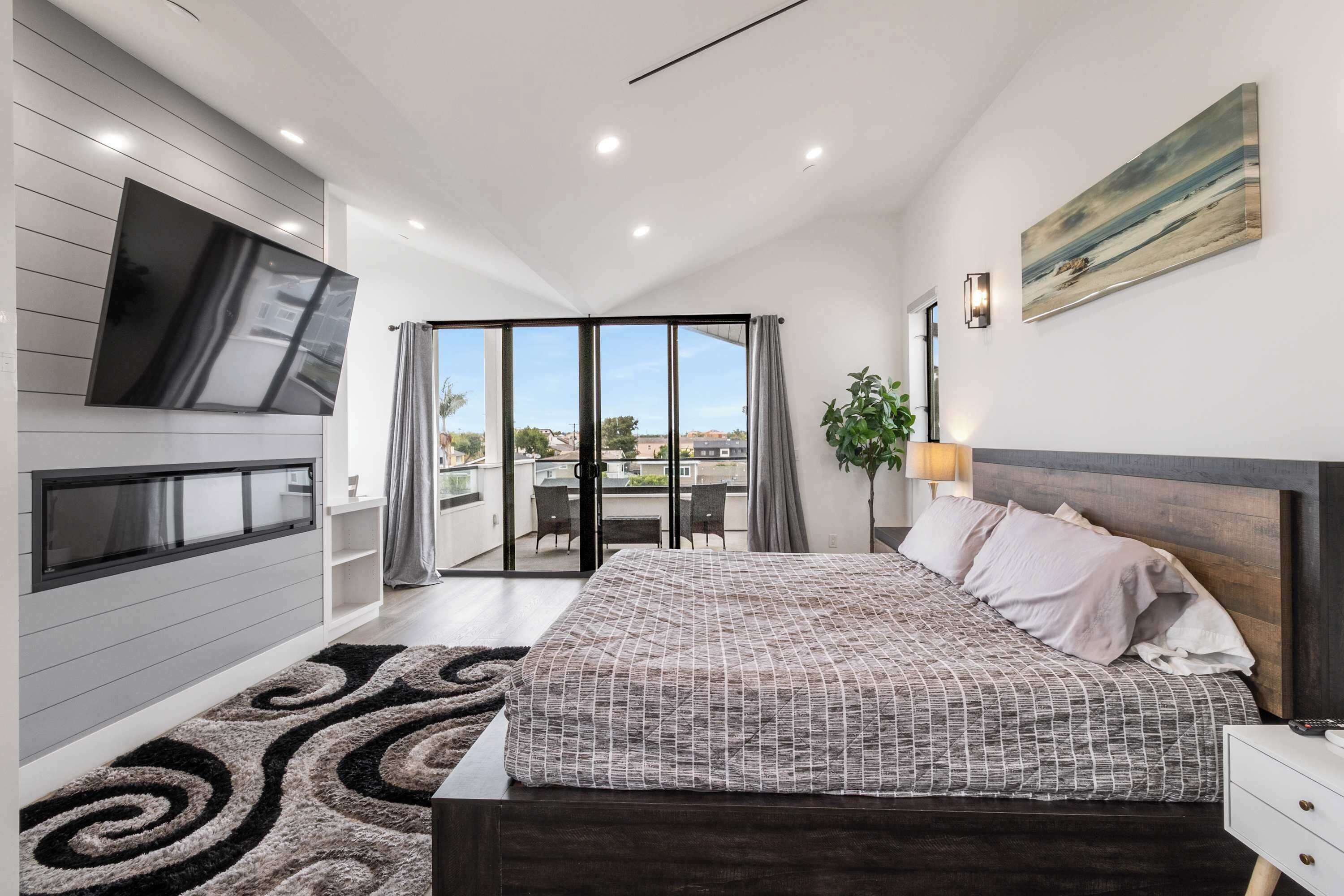 Quarto moderno com uma cama grande, uma TV na parede, uma varanda com vista e uma porta deslizante para área externa.