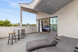 Un patio moderno al aire libre con una silla de salón, dos taburetes de bar y una mesa.