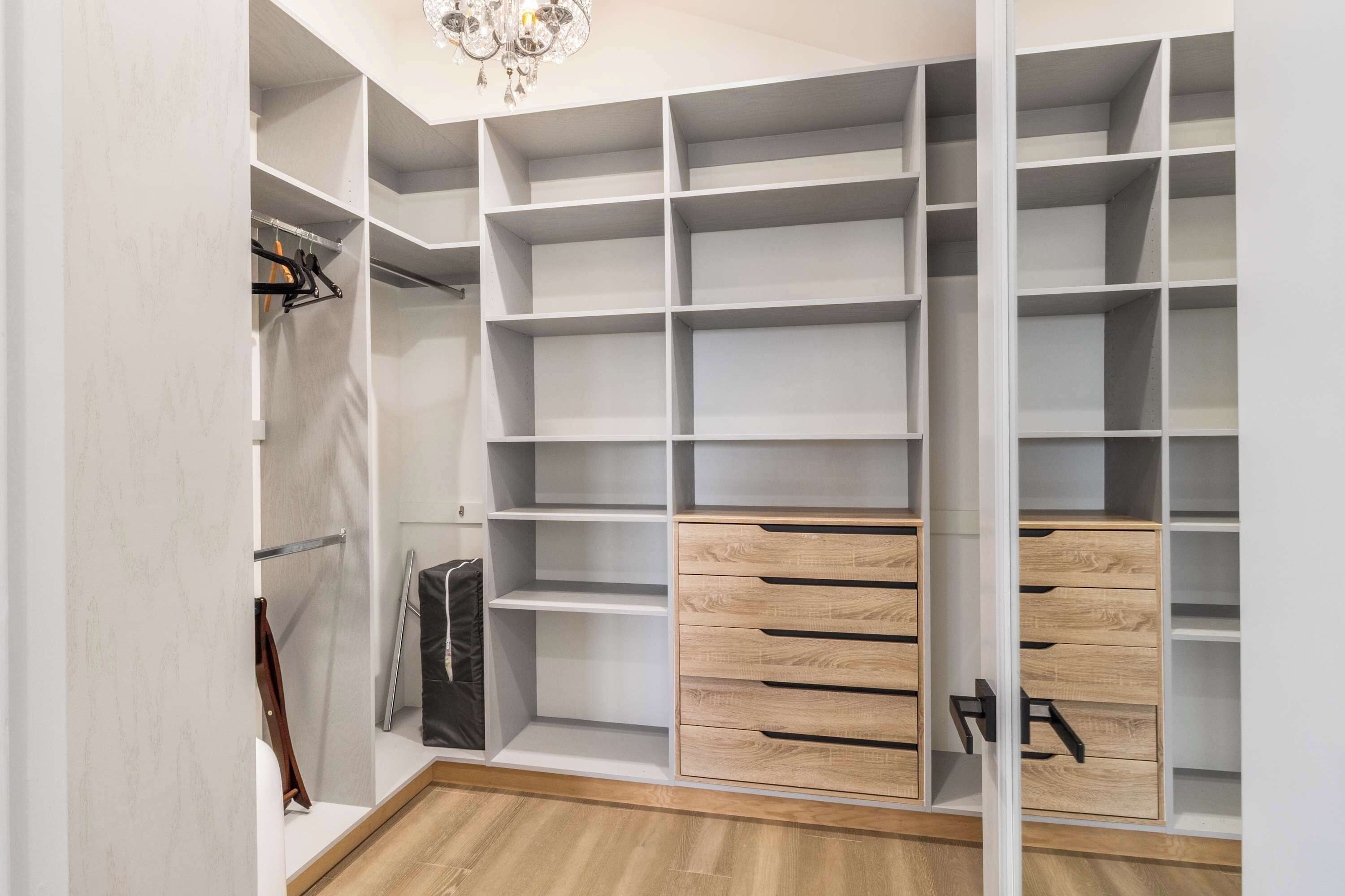 A walk-in closet with multiple shelves and drawers, a coat rack, and a chandelier.