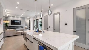 A modern kitchen with a marble countertop, stainless steel appliances, and pendant lighting. - @ Marbella Lane - Luxe 4BR Haven w/ Skyscape Views (Huntington Beach)