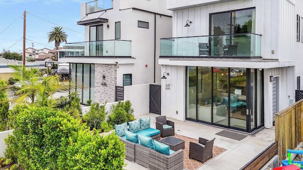 A modern two-story house with a balcony, a patio with outdoor furniture, and a well-maintained garden. - @ Marbella Lane - Luxe 4BR Haven w/ Skyscape Views (Huntington Beach)