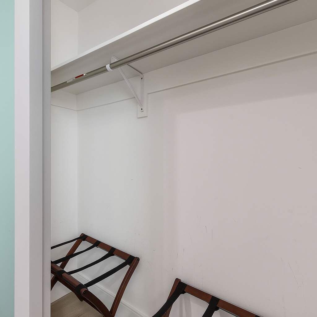 A room with a white wall, a wooden bench, and a metal rod.