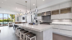 A modern kitchen with a large island, stainless steel appliances, and a view to the outdoors. - @ Marbella Lane - Luxe 4BR Haven w/ Skyscape Views (Huntington Beach)