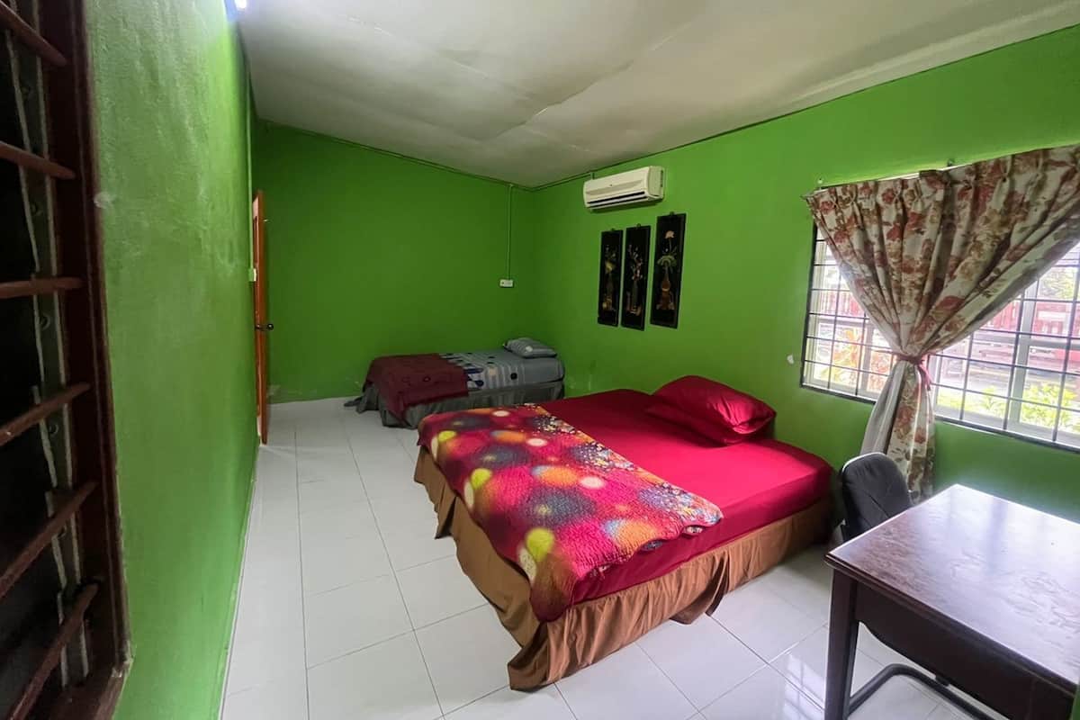 A room with green walls, a bed with a colorful blanket, a desk, and a window with curtains.