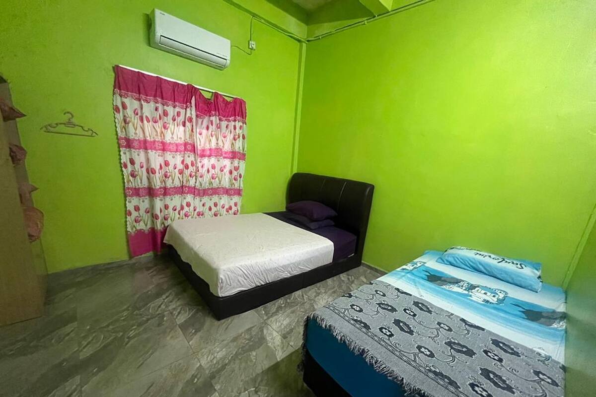 A room with two beds, a window with pink and white curtains, and a green wall.