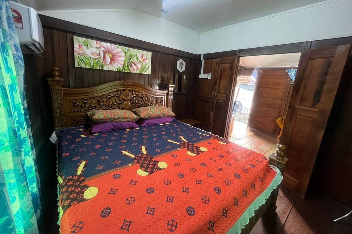 A bedroom with a wooden bed, floral artwork on the wall, and a view of the outside through an open door.
