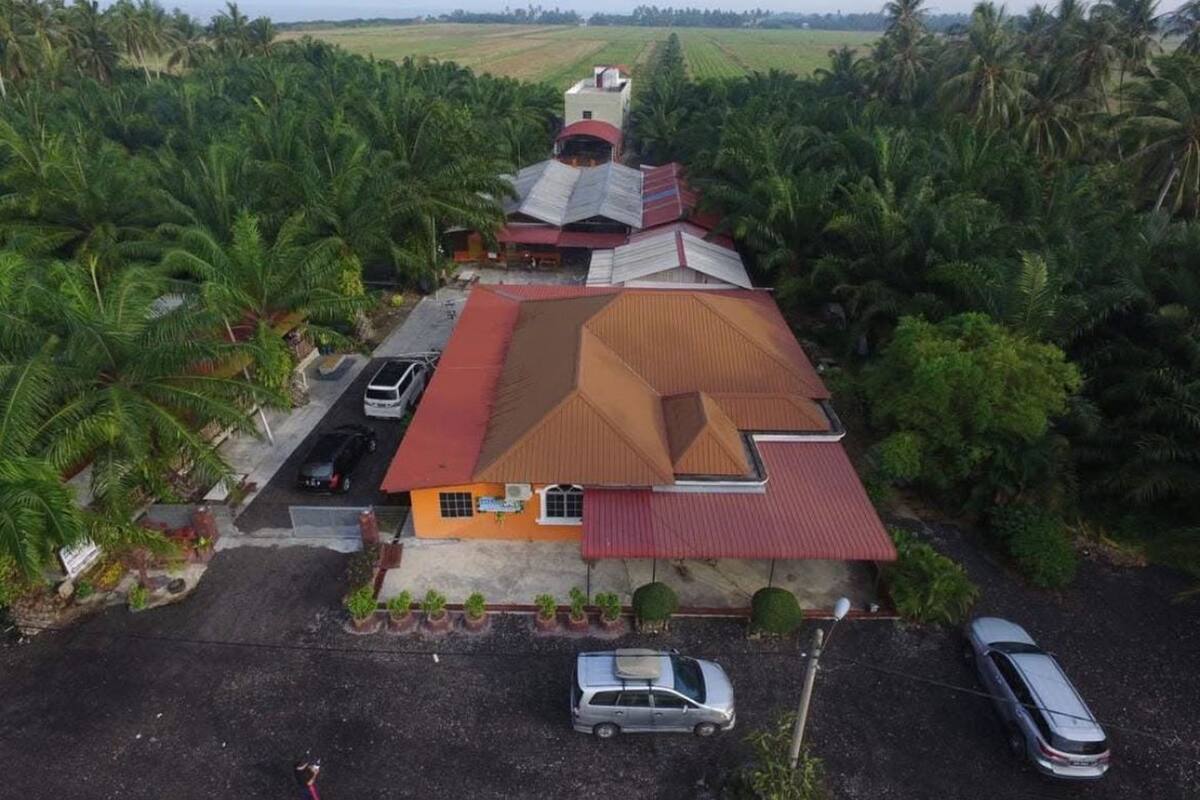 A single-story building with a red roof, surrounded by palm trees, and a parking area with two cars.
