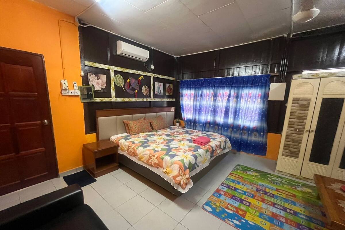 A bedroom with a bed, a wardrobe, a small table, a colorful rug, and a wall-mounted air conditioner.