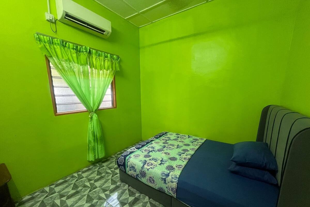 A small room with a single bed, a window with green curtains, and a geometric patterned floor.