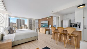 Ein modernes Hotelzimmer mit einem großen Bett, einer Essecke mit Barhocker, einer Küche und Blick auf die Stadt.