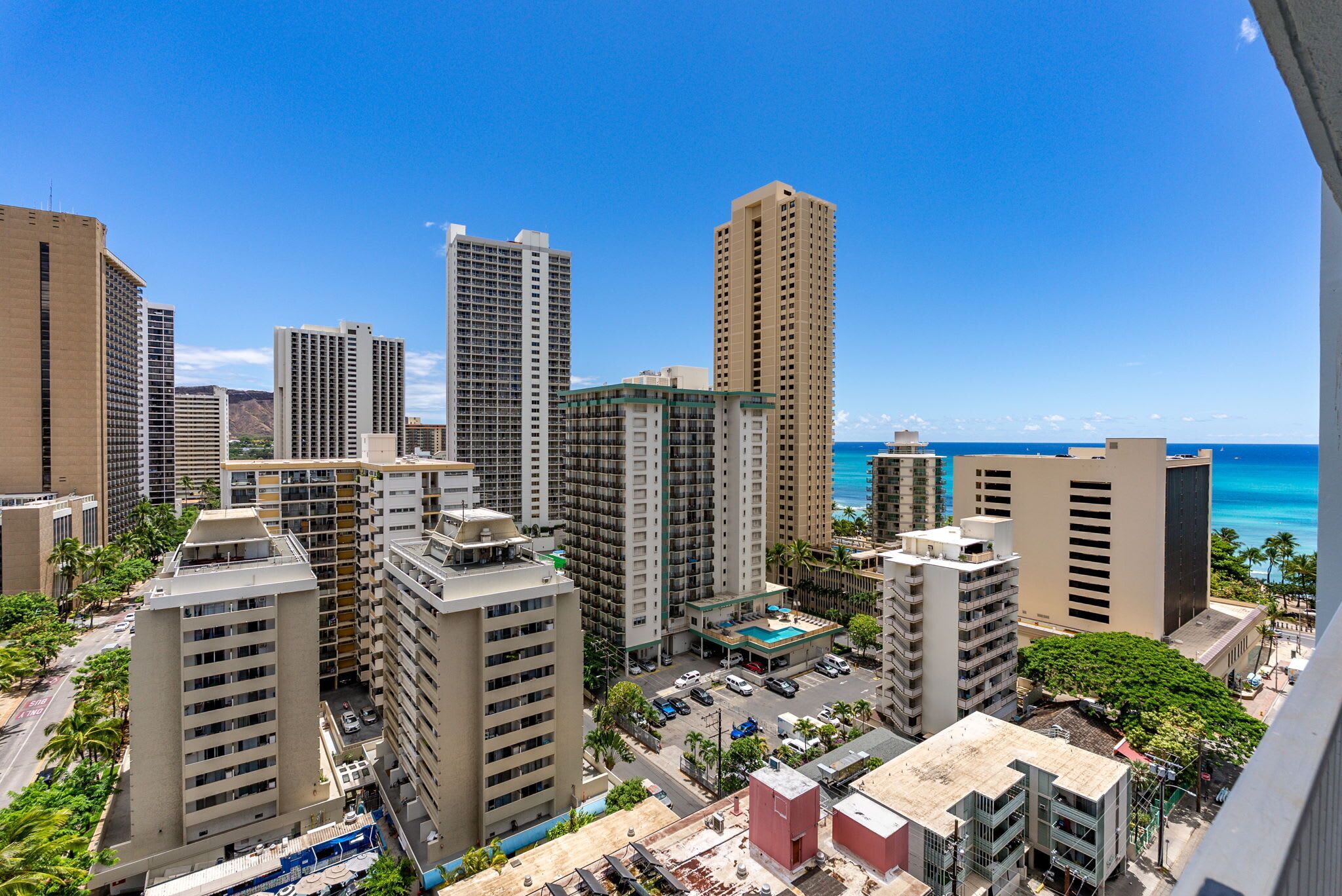 A high-rise hotel with multiple floors, a parking area, and a view of the ocean.