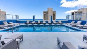 Ein Pool auf dem Dach mit Liegestühlen und Blick auf das Meer und die Gebäude.
