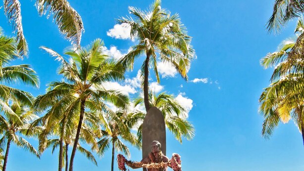 Ein Strand mit Palmen, einer Statue und Strandstühlen.