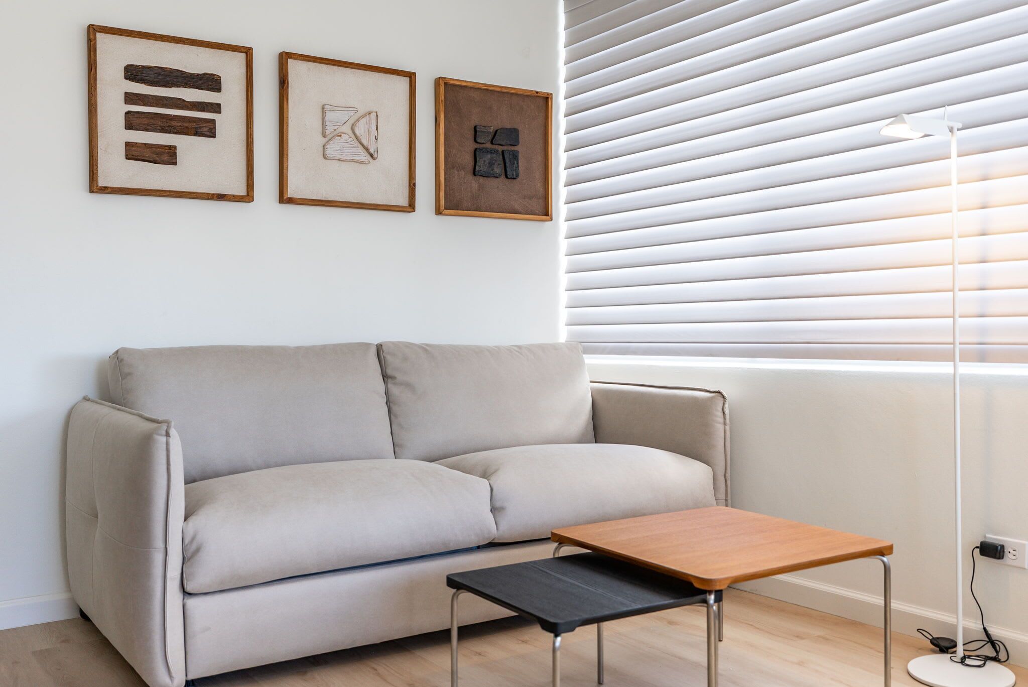 Una sala de estar moderna con un sofá color beige, una mesa de centro de madera y tres obras de arte enmarcadas en la pared.