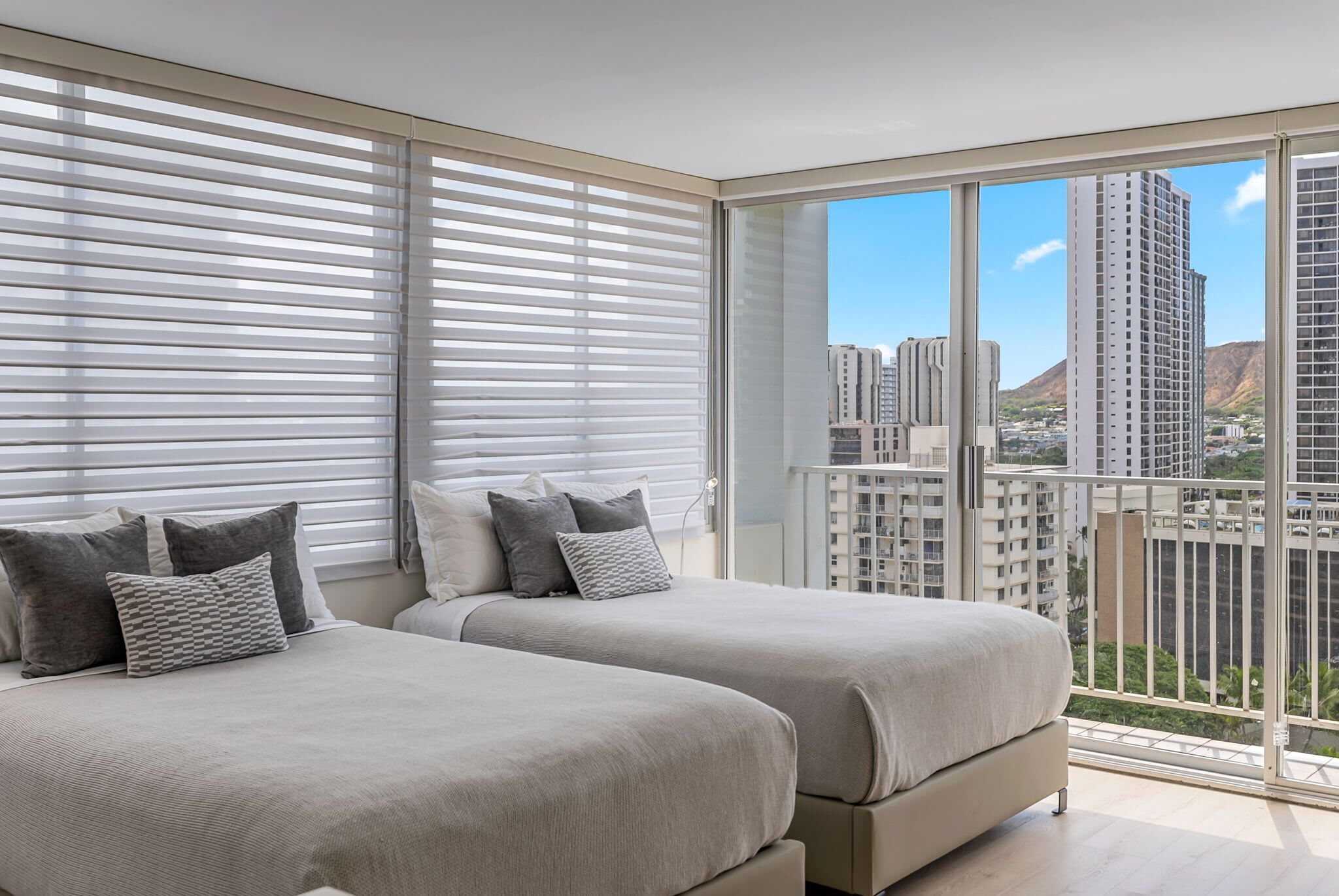 Una camera da letto moderna con due letti, ampie finestre e vista sugli edifici della città.