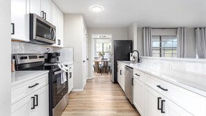 A modern kitchen with white cabinets, stainless steel appliances, and a wooden floor.