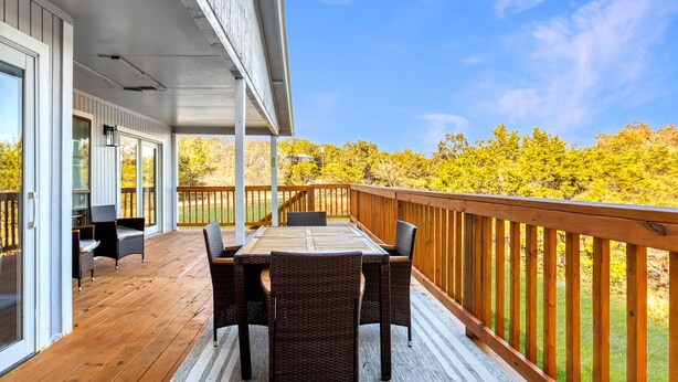 A covered patio with a wooden deck, a table with chairs, and a view of trees and sky.