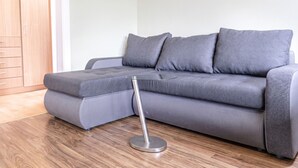 A grey sectional sofa with a glass coffee table, wooden flooring, and a wooden door in the background. - Comfy Room in Shared Villa w/ Free Parking (Wien)