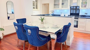 A modern kitchen with white cabinets, a central island, and blue chairs around a dining table set for four.