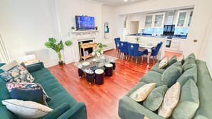 A modern living room with a green sofa, a dining table, and a kitchen in the background.