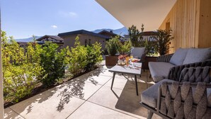 Un patio con mesa y dos sillas, rodeado de plantas en macetas y vistas a casas y montañas.