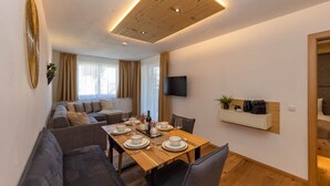 Una sala de estar moderna con comedor, un conjunto de sofás, un televisor montado en la pared y techo de madera.