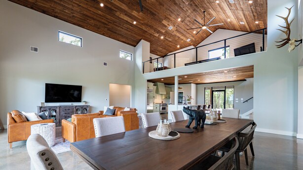Amplia sala de estar con una gran mesa de comedor de madera, sillas blancas tapizadas, un conjunto de sofá y un televisor montado.