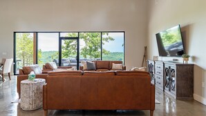 Una sala de estar moderna con un sofá seccional grande, un televisor sobre un mueble bajo y vistas al exterior a través de ventanas amplias.