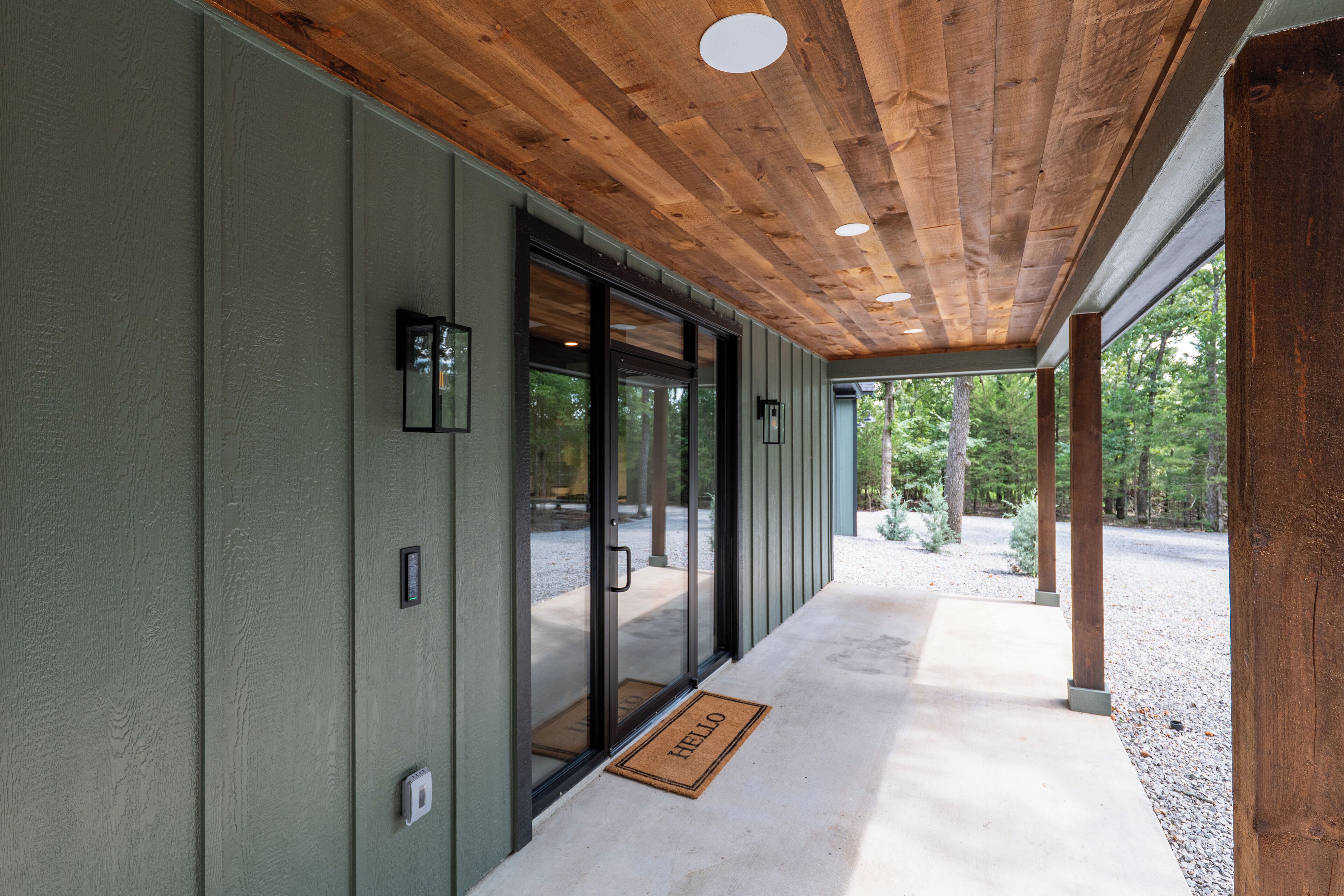 Une allée couverte avec des poutres en bois au plafond, des portes vitrées et un paillasson.