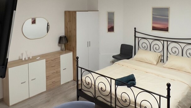 A bedroom with a bed, a desk, a chair, a wardrobe, and a round table with flowers.