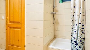 A bathroom with a wooden door, a shower with a curtain, and a small shelf with toiletries.