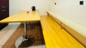 A room with a long wooden table, a bench, and a dark-colored kettle.