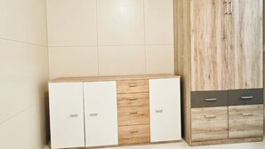 A room with a white tiled floor, a wooden cabinet with drawers, and a white cabinet with handles.