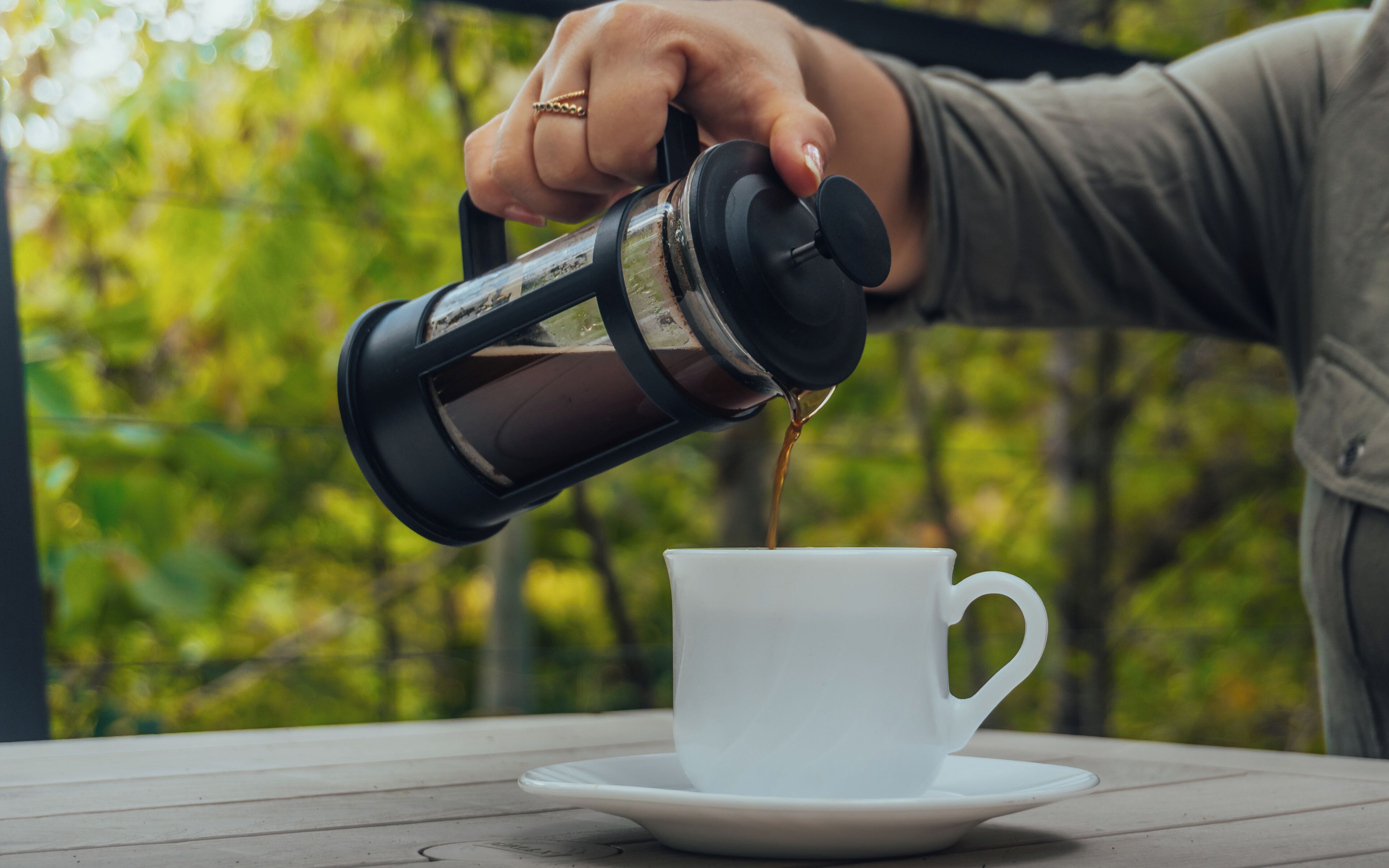 Eine Hand gießt Kaffee in eine weiße Tasse auf einem Untertasse.
