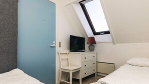 Un dormitorio con techo inclinado, un televisor sobre una cómoda y dos camas.
