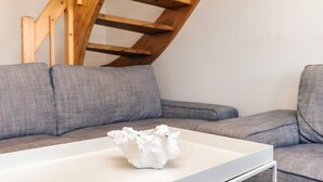 Una sala moderna con una mesa de centro blanca, sofás grises y una escalera de madera.