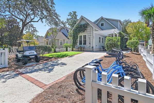A residential driveway with a golf cart, a bicycle rack, and houses in the background.