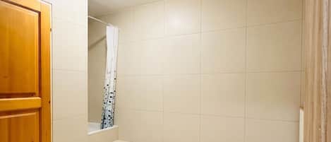 A bathroom with a wooden door, tiled walls, and a shower area.