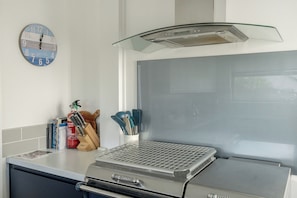 A kitchen with a stainless steel range hood, a clock on the wall, and various kitchen utensils on the counter.