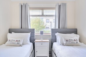 A twin room with two beds, a nightstand, a lamp, and a window with curtains.