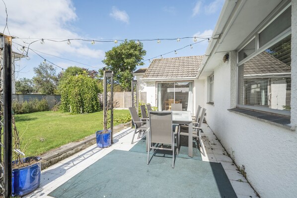 A patio with a table and chairs, a blue mat, and a garden view.