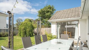 Un patio con una mesa y sillas de vidrio, rodeado de un jardín y una casa con tejado de tejas.