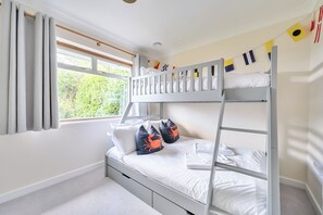 Une chambre avec un lit superposé, une fenêtre, des rideaux et une vue sur la verdure environnante.